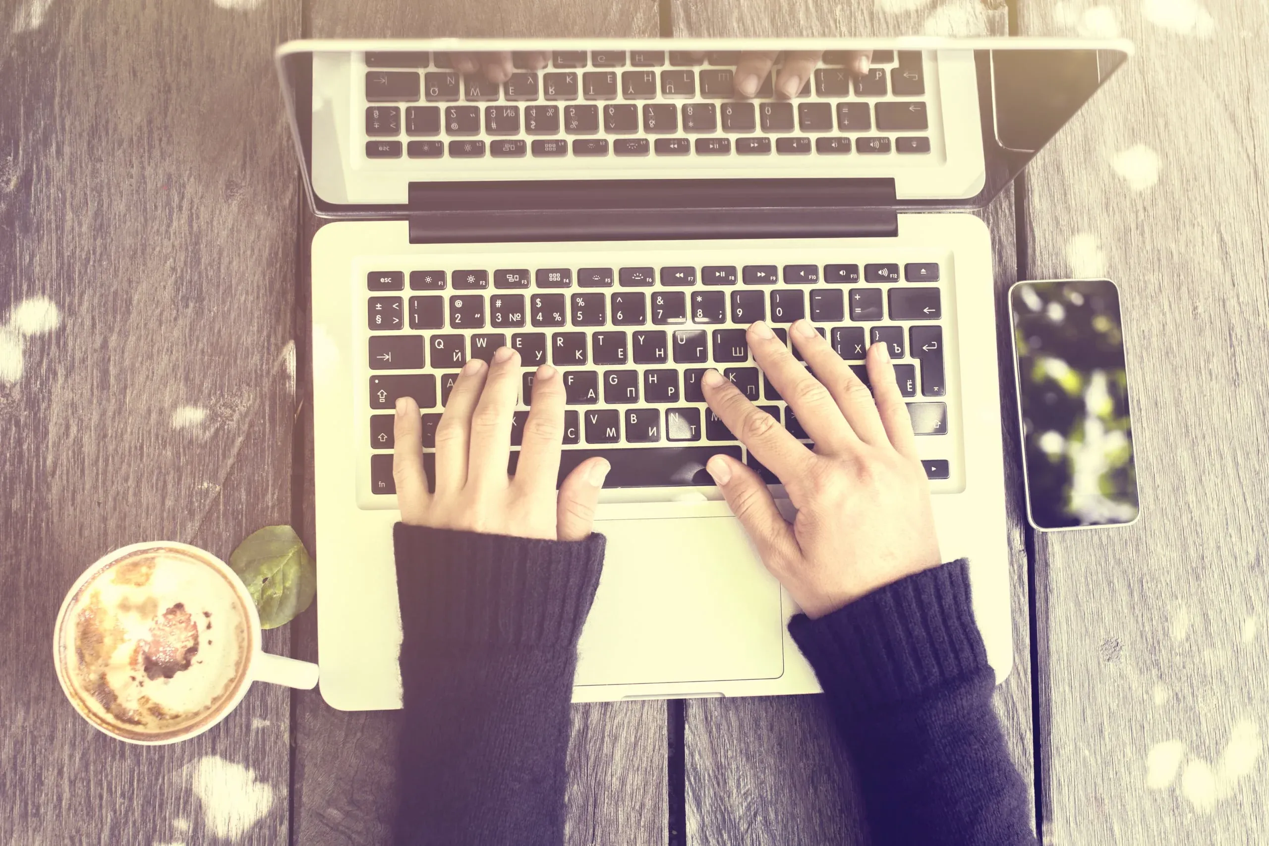 mains entrain de taper sur les touches de clavier d'un ordinateur portable. Café et cellulaire visibles sur l'image